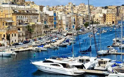 Malta historia: malowniczy port pełen jachtów, z zabytkową zabudową w tle.