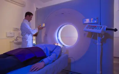 Arzt bedient CT-Scanner, Patient liegt auf Liege. Die CT-Strahlenbelastung wird minimiert.