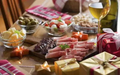 Domowe menu na sylwestra: deska wędlin i serów, oliwki, sałatka caprese, orzechy, wino i prezenty.