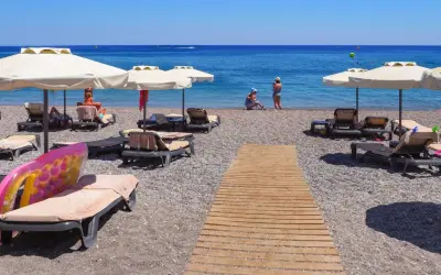 Słoneczny kurort nad Morzem Czarnym. Leżaki pod parasolami, drewniana ścieżka na kamienistej plaży, ludzie kąpiący się w morzu.