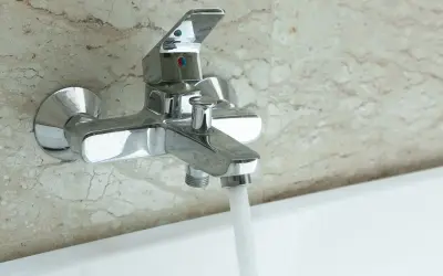 Robinet de baignoire mural chromé, prêt à installer, avec eau coulant doucement.