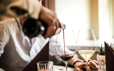 Versando vino rosso in un calice, scoprendo il significato di vino fermo. Accanto, un bicchiere di vino bianco.