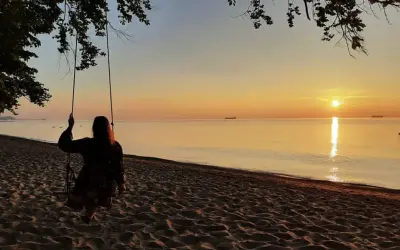 Zachód słońca nad morzem, dziewczyna na huśtawce na plaży.
