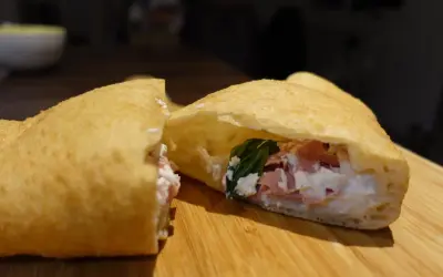 Une pizza frite napolitaine, garnie de ricotta, jambon et basilic, sur une planche en bois.