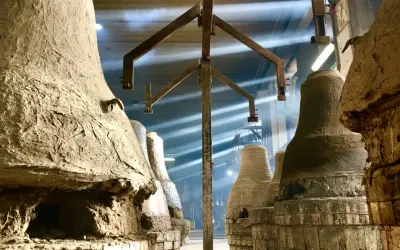 Forni antichi nel paese delle campane Molise, con raggi di luce che illuminano la polvere e le forme grezze delle campane in attesa di essere fuse.