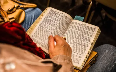 Osoba czyta Biblię, skupiając się na psalm 9. W tle widać torebkę i fragmenty ubrania.