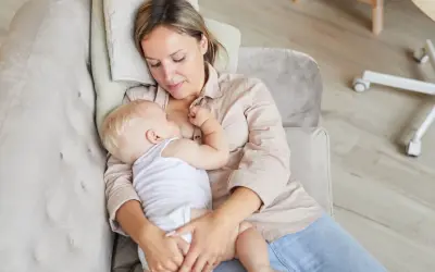 Ciepłe chwile karmienia spod pachy. Mama tuli dziecko, karmiąc je piersią na kanapie.