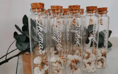 Bouteilles en verre avec fleurs séchées, bouchons en liège et breloques dorées. Parfait cadeau invité bapteme diy personnalisé avec des prénoms.