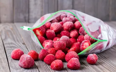 Mrożone truskawki wysypują się z otwartej torebki. Idealne, by rozmrażać truskawki do galaretki.