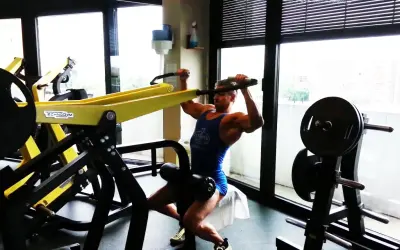 Uomo muscoloso esegue esercizi dorsali macchinari Technogym, concentrato sul movimento.