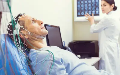 Pacjent leży z elektrodami na głowie podczas badania EEG. Czy badanie eeg czy boli? Nie, jest bezbolesne. Lekarka analizuje wyniki.