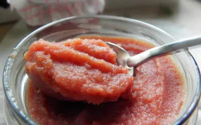 Łyżeczka zanurzona w słoiku z gęstym, różowym curd wiśniowym. Idealny dodatek do deserów.