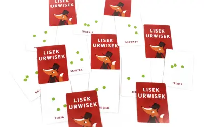 Karty z gry "Lisek Urwisek grają" rozsypane na białym tle. Wesoły lisek w cylindrze zachęca do zabawy.