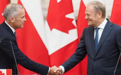 Dwóch polityków ściska sobie dłonie na tle flag Kanady. Wzmocnienie relacji polska-kanada.