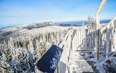Zimowe krajobrazy Beskidów z wieży widokowej. Śnieg pokrywa drzewa i balustrady, tworząc malownicze widoki. To jedne z wielu atrakcji Beskidów zimą.