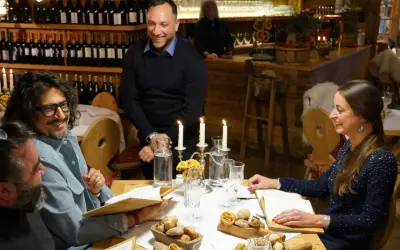 Un gruppo di amici ride a tavola in un ristorante di Milano, tra candele e bottiglie di vino.