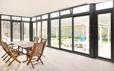 Comedor interior con mesa de madera y sillas, conectado a un jardín con porche acristalado. Precio a consultar.