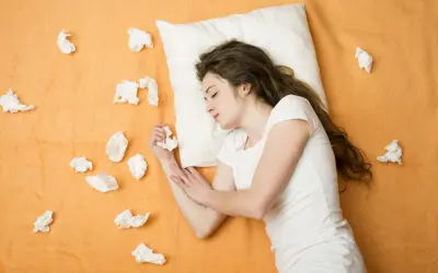 A young woman sleeps on a pillow surrounded by crumpled tissues, suggesting she might sneeze in her sleep.