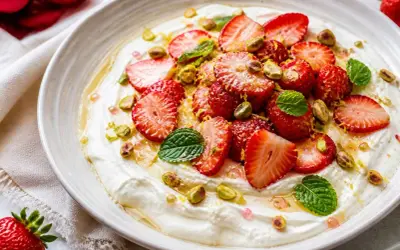Délicieuse salade de fruits maison : fraises fraîches, pistaches croquantes et menthe fraîche sur une crème onctueuse, arrosée de miel.