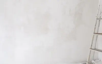 Étape de nettoyage d'un mur blanc jauni, une échelle est visible sur la droite.