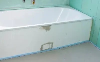 Einbau einer neuen, weißen Badewanne in einem Badezimmer im Rohbau. Grüne Gipskartonplatten und vorbereitete Rohre sind sichtbar.
