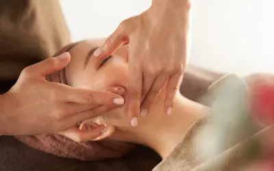 Manos expertas realizan un **dibujo masaje facial paso a paso**, aplicando suaves presiones en el rostro de una mujer para relajarla.