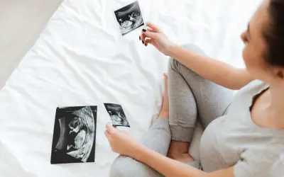 Kobieta w ciąży ogląda zdjęcia USG płodu na białym łóżku.