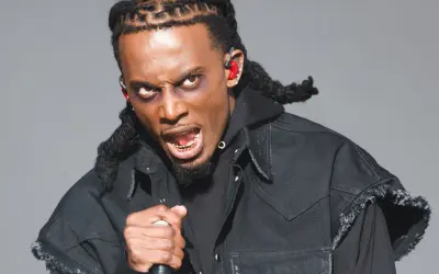 Playboi Carti z mikrofonem, w czarnej kurtce i z charakterystycznymi warkoczami. Jego ekspresja sugeruje energię znaną z jego playboi carti utworów.