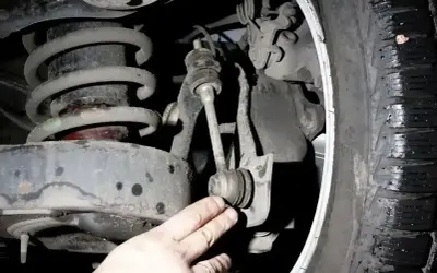 Dłoń mechanika wskazuje na zużyte tuleje stabilizatora w zawieszeniu samochodu.