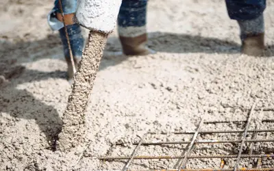 Beton wylewany z rury na zbrojenie, w tle widać nogi w gumowcach.