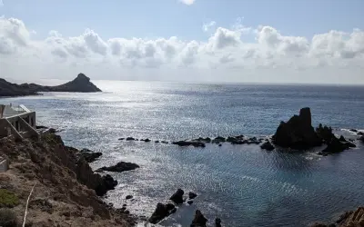 Costa rocosa con formaciones volcánicas emergiendo del mar azul. El arrecife San José se alza majestuoso, reflejando el sol.