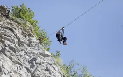 Człowiek zjeżdża na tyrolce obok skalnej ściany z ubezpieczeniami, jak na via ferrata polska.