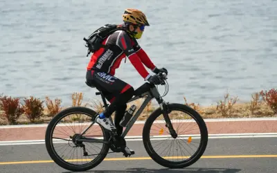 Rowerzysta w kasku i masce jedzie rowerem wzdłuż jeziora. Idealne noclegi dla rowerzystów czekają po wyczerpującej trasie.