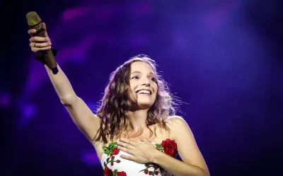 Sanah śpiewa "Bujda" na koncercie, trzymając złoty mikrofon i dotykając serca.
