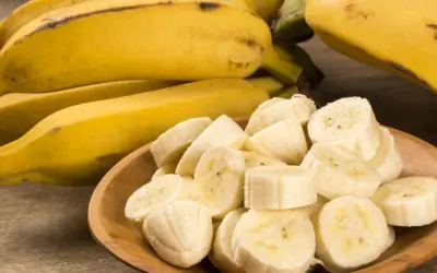 Kawałki banana na drewnianej misce, obok całe owoce. Idealna przekąska, gdy zastanawiasz się nad banan kcal.