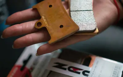 Main d'une personne tenant des plaquettes de frein neuves, prêtes pour le rodage. Le logo "DZ" est visible sur l'une d'elles.
