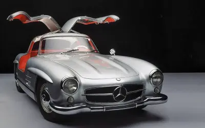 Srebrny Mercedes 300SL z otwieranymi do góry drzwiami, z czerwonym wnętrzem, prezentuje się elegancko na ciemnym tle.