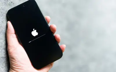 Dłoń trzyma iPhone'a z logo Apple i paskiem postępu. To może być wskazówka, jak wyczyścić pamięć w iPhone, gdy system się ładuje.