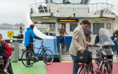 Man met fiets op veerboot, een ongeluk fietser in de verte.