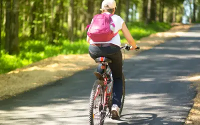 Osoba na rowerze z plecakiem jedzie leśną ścieżką. To świetny sposób, jak jeździć na rowerze żeby schudnąć.
