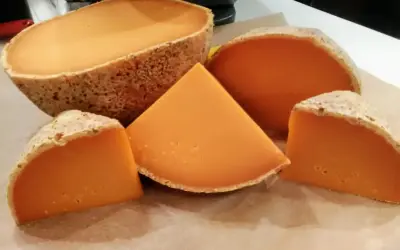 Un queso mimolette peligroso, con su corteza rústica y su vibrante interior anaranjado, se presenta en cuñas y una pieza entera, invitando a una degustación audaz.