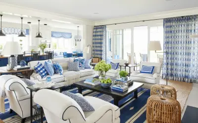 A bright living room with coastal interior design, featuring white sofas, blue and white patterned pillows, and a dark wood coffee table.