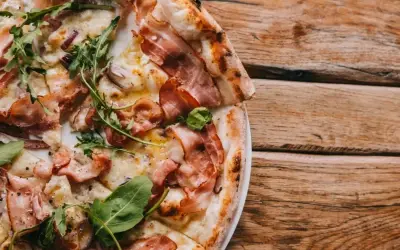 Pyszna pizza carbonara z chrupiącym boczkiem i rukolą, podana na drewnianym blacie.