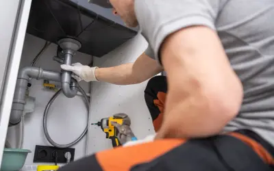Plombier ajustant une canalisation PVC sous un évier. Outils à portée de main pour le dépannage.