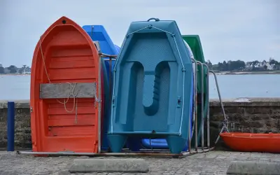 Plusieurs petites embarcations colorées, dont une annexe orange, sont rangées sur le quai, face à la mer.