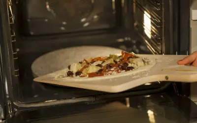 Pizza z dodatkami na łopacie do pizzy, gotowa do wsunięcia na kamień do pizzy granitowy w rozgrzanym piekarniku.