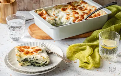 Pyszne lasagne ze szpinakiem, zapieczone na złoto, podane na talerzu obok szklanki wody z cytryną.