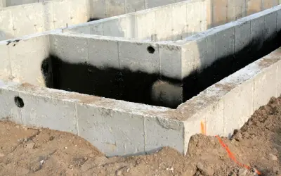 Betonowe bloczki zalewowe tworzą fundament domu, zabezpieczone czarną izolacją przeciwwilgociową.