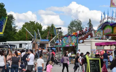 Buntes Treiben auf einem Volksfest mit Fahrgeschäften und vielen Besuchern. Ein Schiff-Karussell dreht sich, während Menschen an Ständen vorbeischlendern.