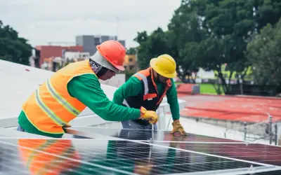 Dwóch pracowników z **świadectwem kwalifikacyjnym e** montuje panele słoneczne na dachu.